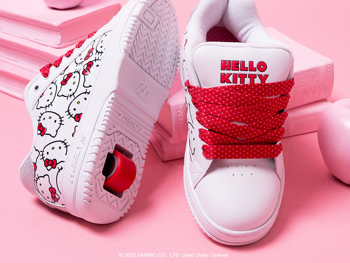 Hello Kitty-themed white Girls Heelys roller shoes with red accents on a pink background