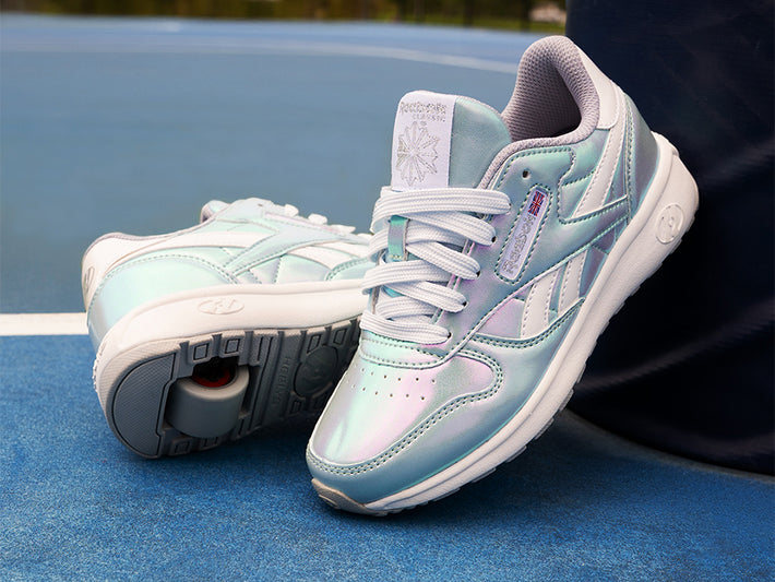 Pair of light blue and white Reebok x Heelys Girls roller shoes on a blue surface