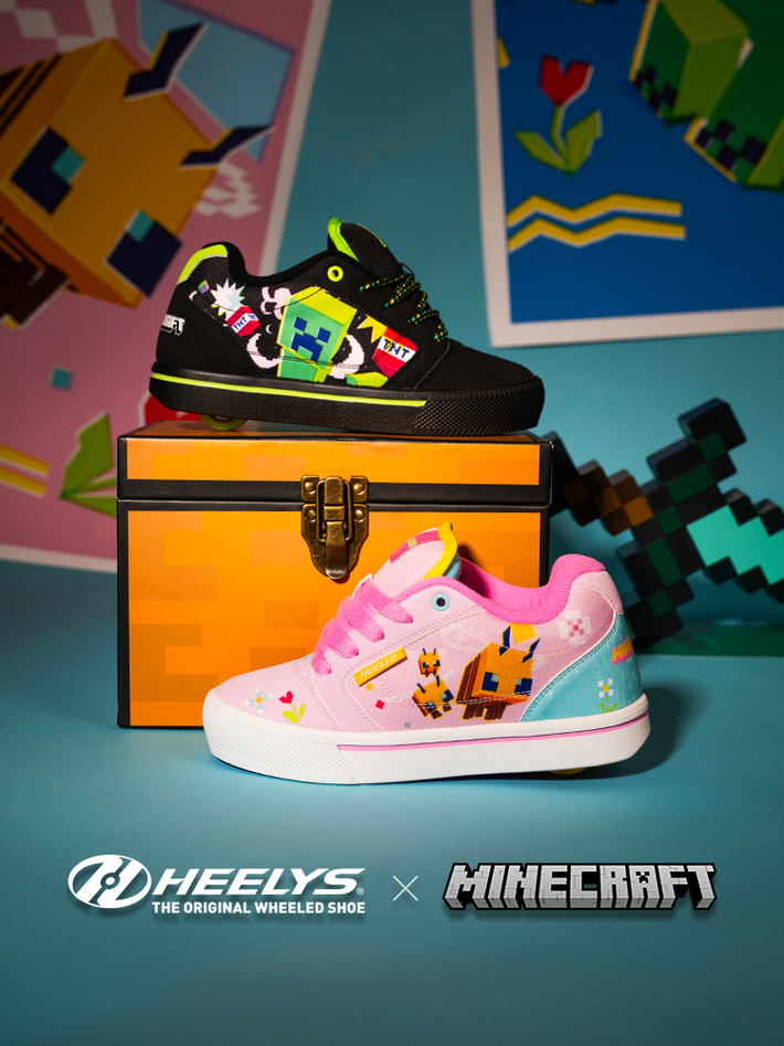 A pair of Heelys x Minecraft roller shoes displayed on a chest. The top shoe is black with colorful creeper graphics, and the bottom shoe is light pink with a white sole and pink laces.