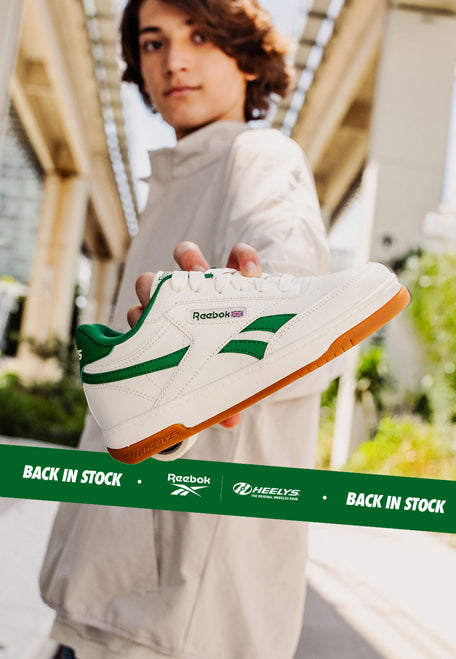 Person holding a white Reebok Heelys roller shoe with green accents outdoors
