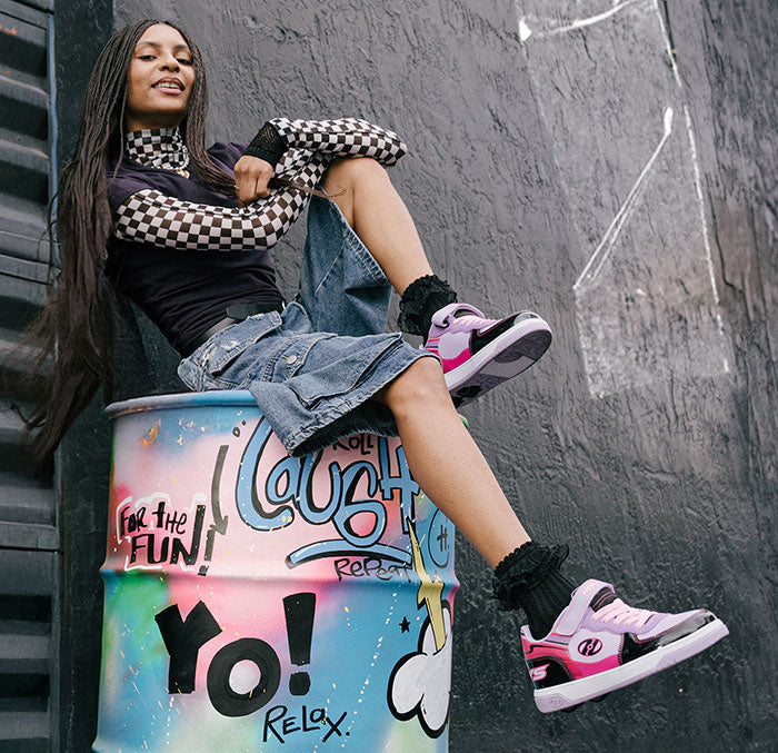 Girls Heelys roller shoes. Person sitting on a colorful barrel, wearing Heelys roller shoes with graffiti against a gray wall
