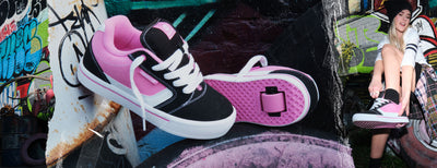 Girls Heelys roller shoes. Black and pink Heelys on a graffiti-covered wall background.